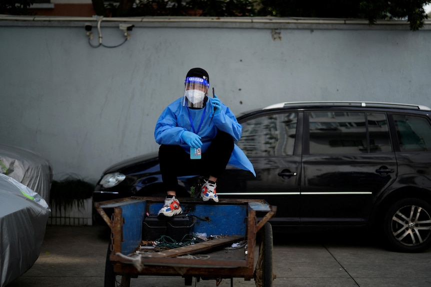 A man in full PPE sits on a rickshaw with his phone to his ear 