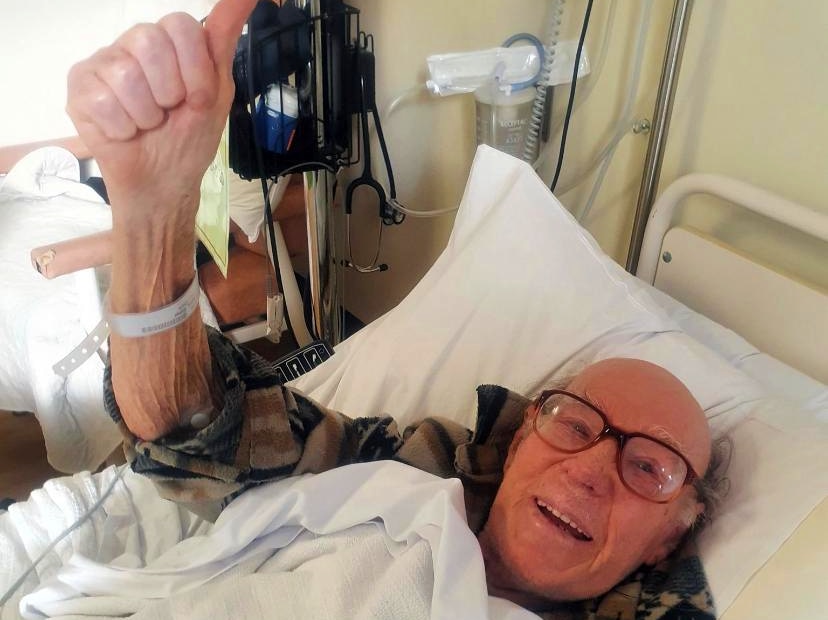 An old man in a hospital bed giving the thumbs up.