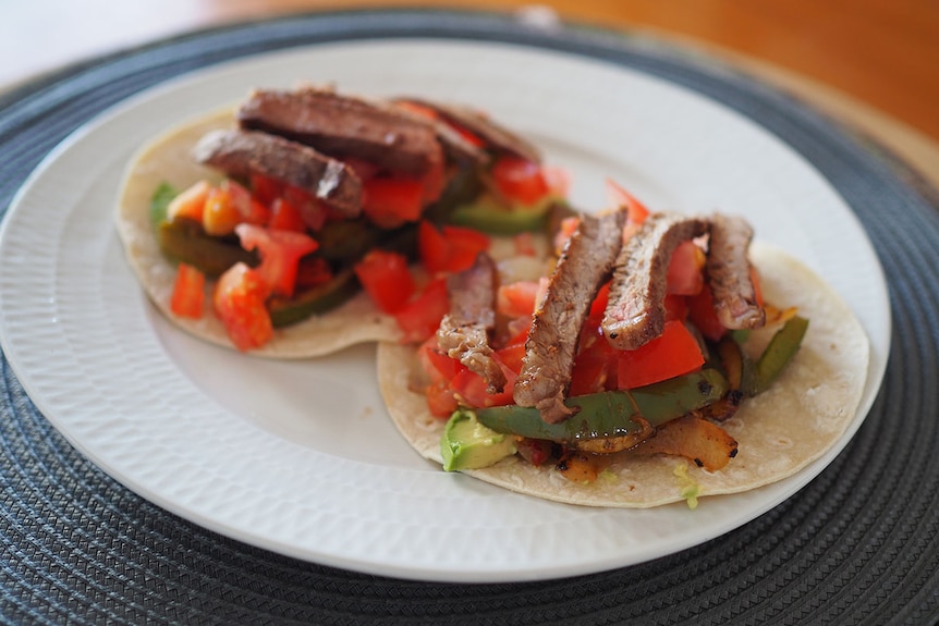 Strips of beef, tomatoes and vegetables sit on two tortilla wraps on a plate.