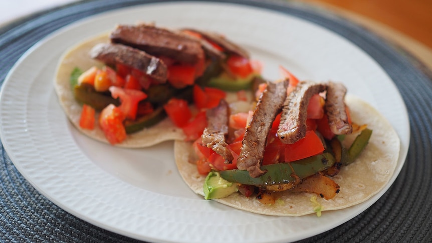 Strips of beef, tomatoes and vegetables sit on two tortilla wraps on a plate.