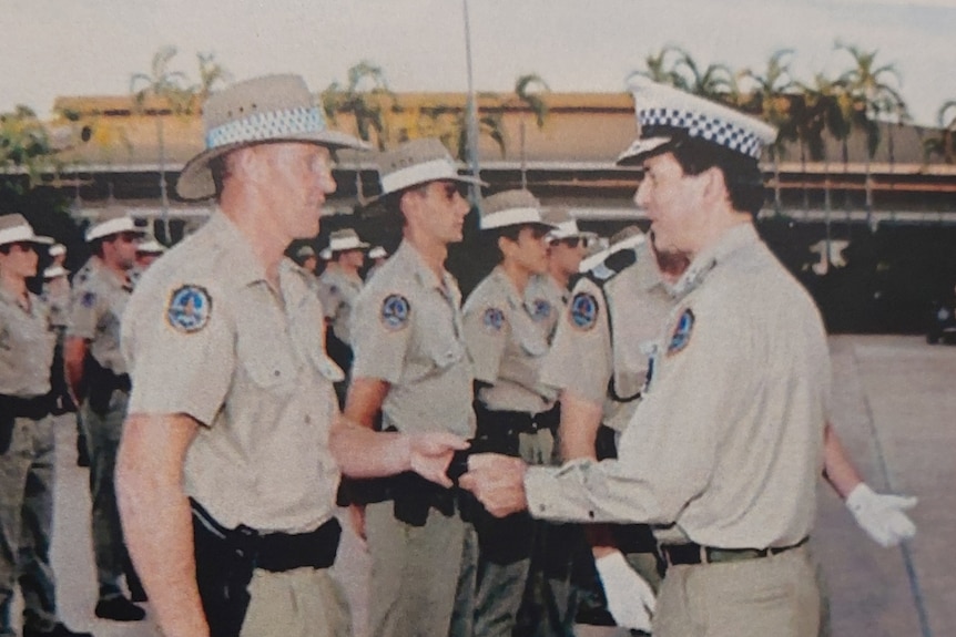 A young police officer shakes hands with his commissioner at a ceremony
