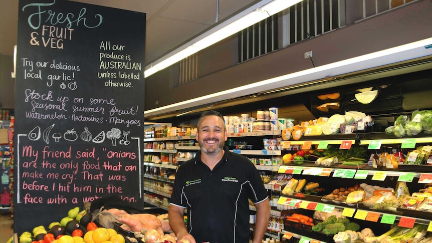 A man stands surrounded by food in a grocery store.