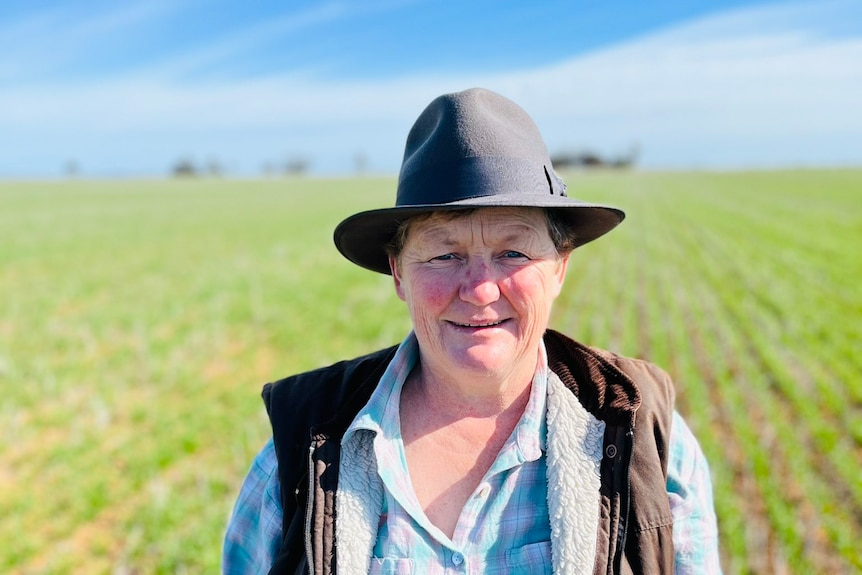 A women in a wide brimmed hat blue shit and and leather vest stands in a green field