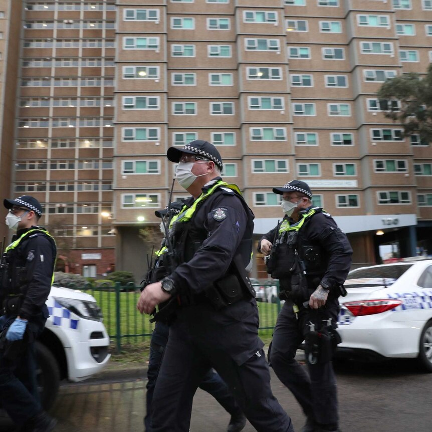 Police wearing face masks walk in front of a public housing block.
