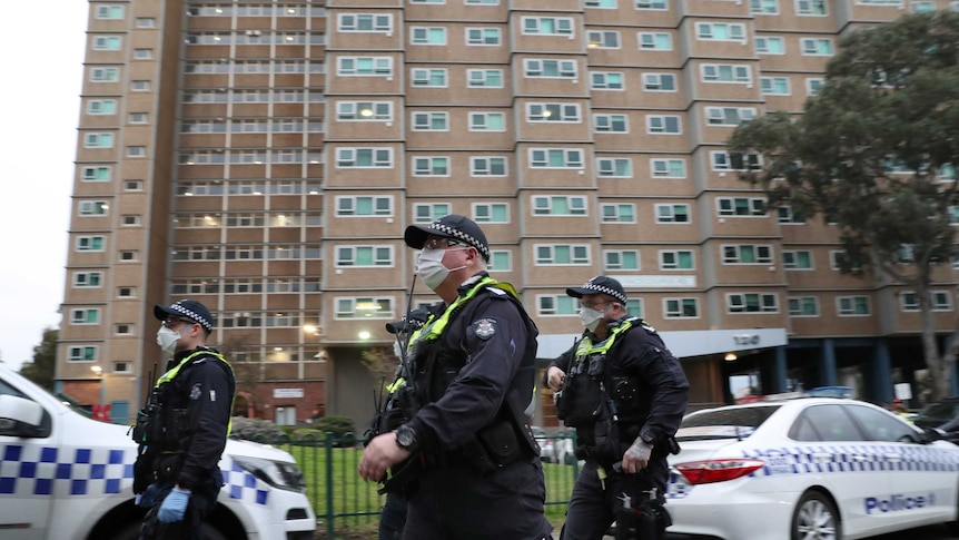 Police wearing face masks walk in front of a public housing block.