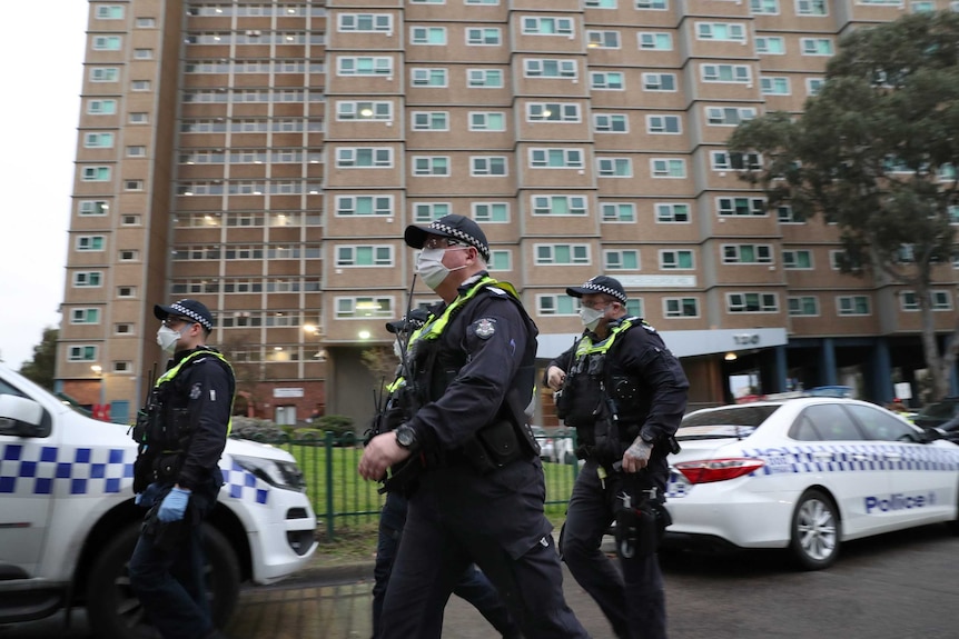 Police wearing face masks walk in front of a public housing block.