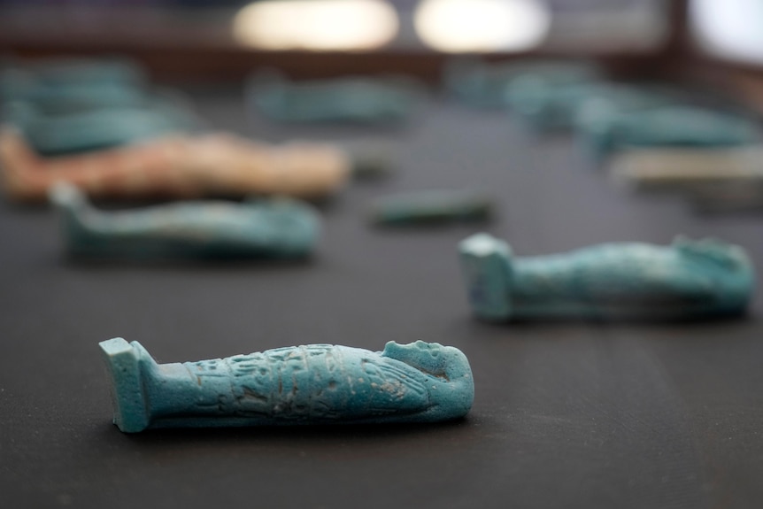 Carved jade mummy pendants lay on a table in rows. 
