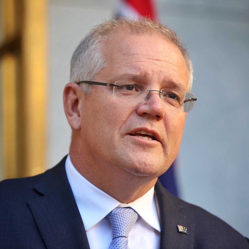 Scott Morrison wears a navy suit and purple tie as he speaks in front of some microphones.