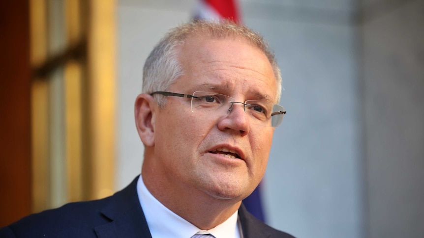 Scott Morrison wears a navy suit and purple tie as he speaks in front of some microphones.