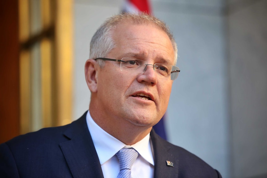 Scott Morrison wears a navy suit and purple tie as he speaks in front of some microphones.