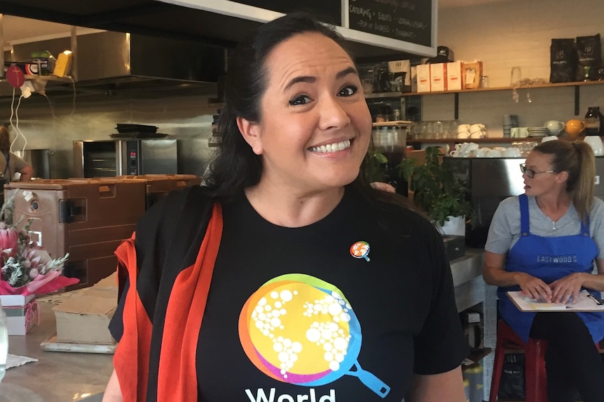 A woman in a World Central Kitchen shirt smiles at the camera standing in a cafe