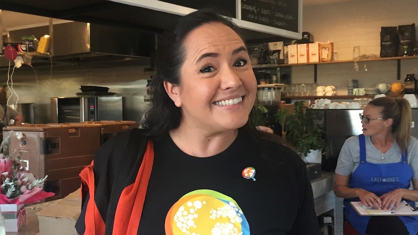 A woman in a World Central Kitchen shirt smiles at the camera standing in a cafe