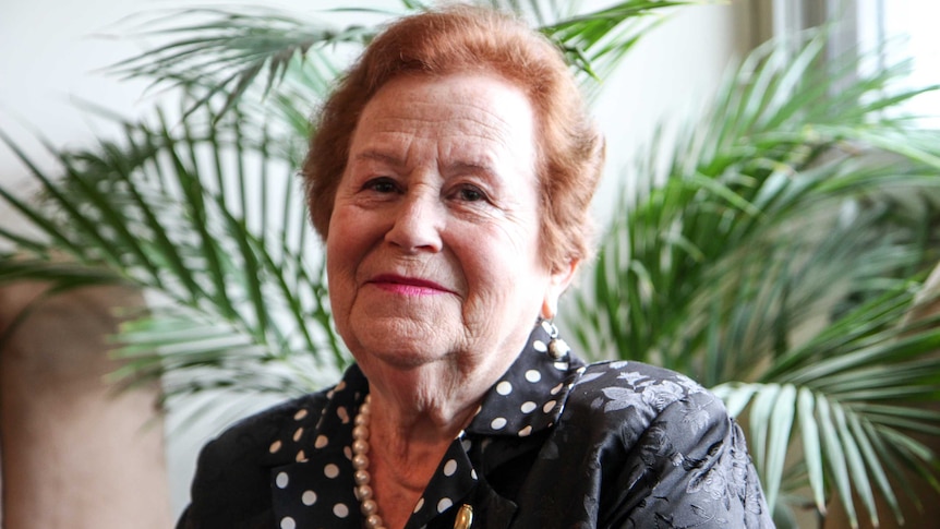 Elderly Jewish woman Yelena Gorodetsky, sits in formal attire. Indoor palm in background.