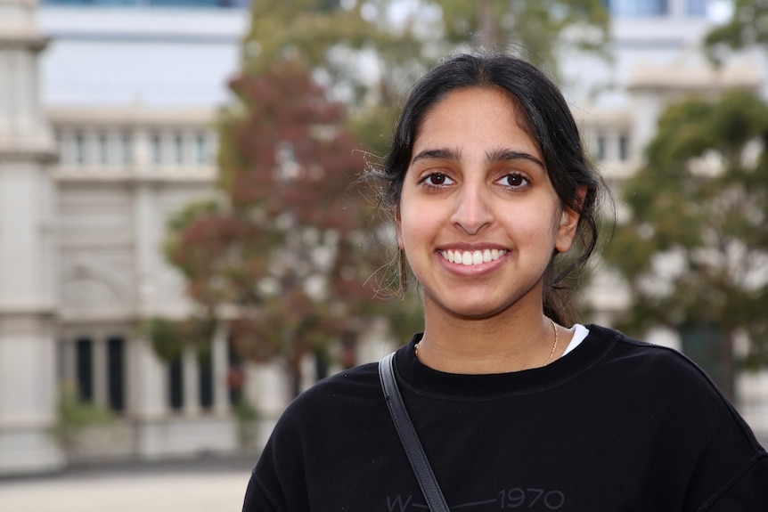 A woman wearing a black jumper smiles and looks straight ahead.