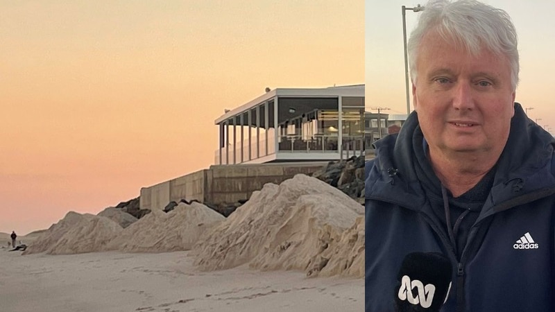 sand piles on beachfront outside surf club at sunrise and grey haired man in track top holding microphone