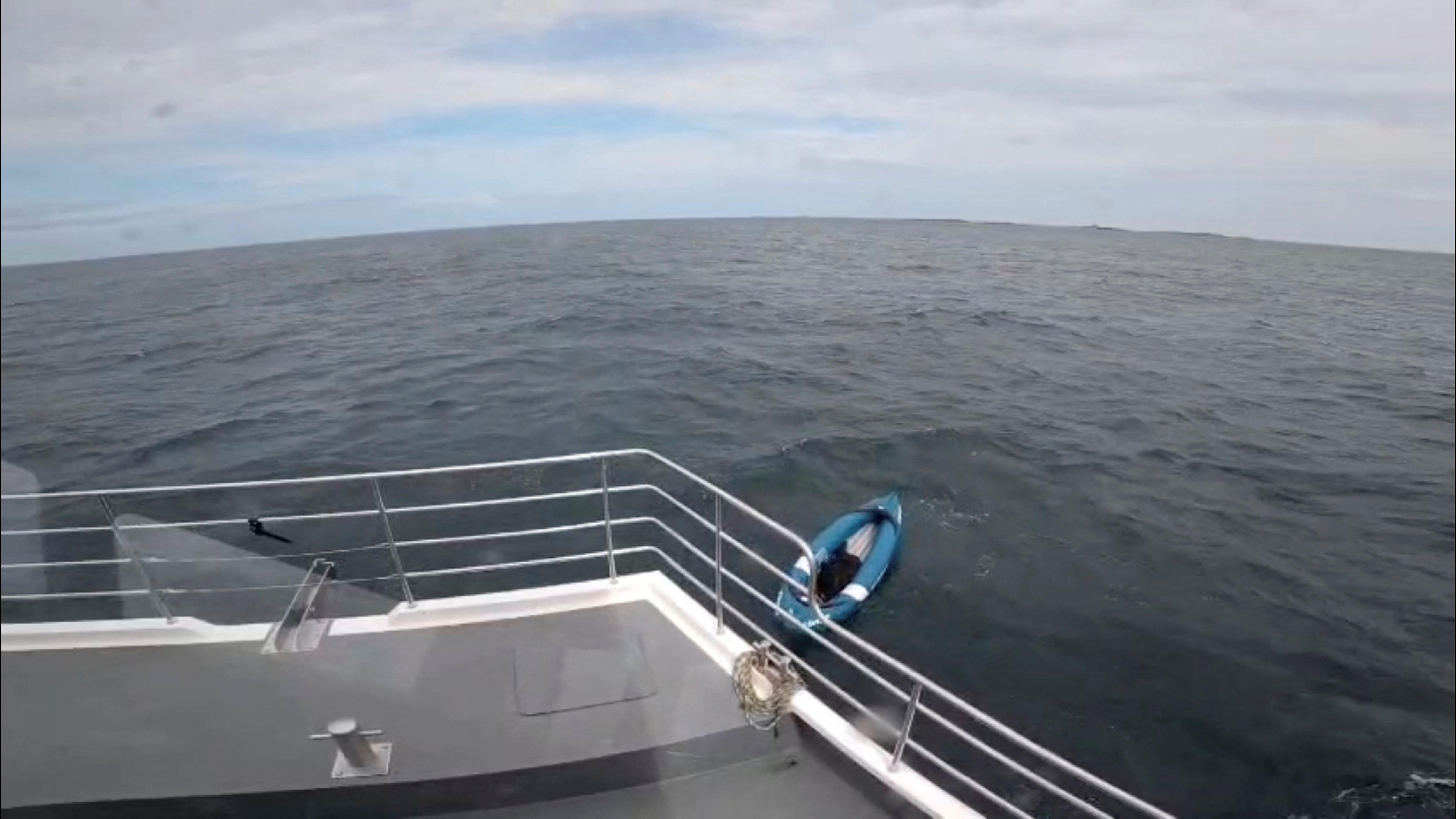 A big black dog inside a blue inflatable kayak floating on the ocean near a boat.