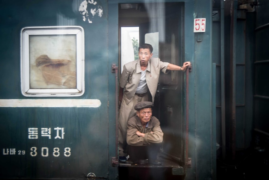 A man crouches while another stands on a train.