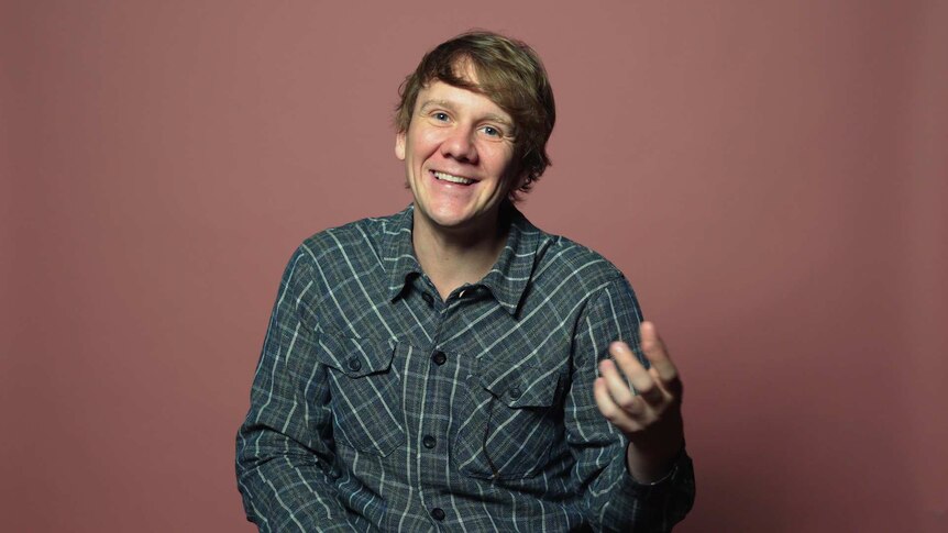 Josh Thomas in front of pink background for a video about his life advice.
