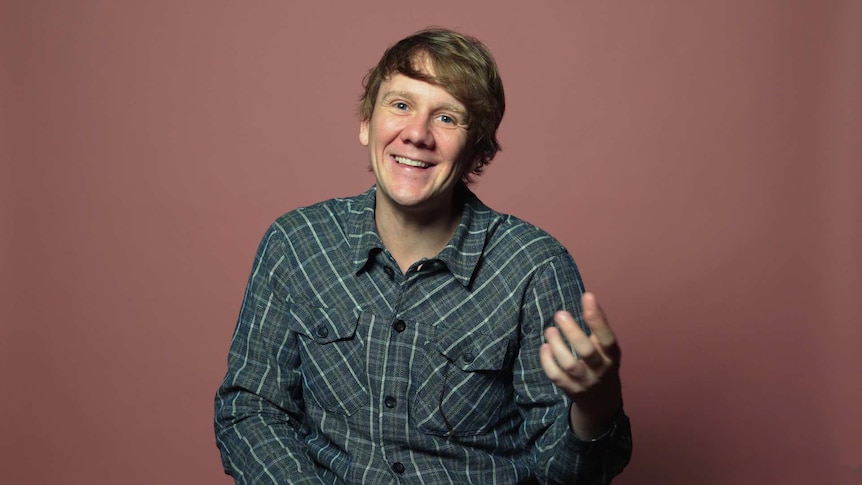 Josh Thomas in front of pink background for a video about his life advice.