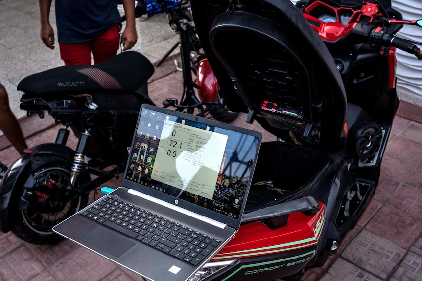 A laptop sits on the back of a red motorbike