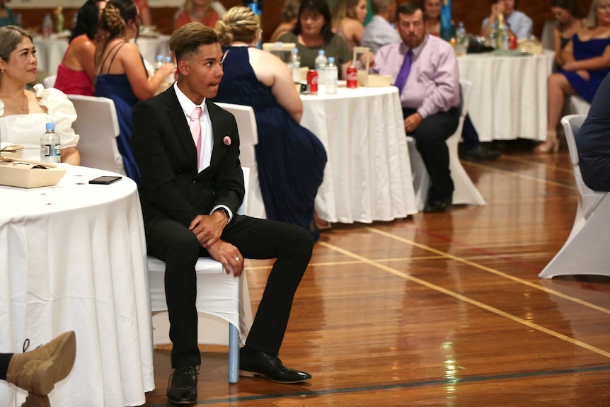 A large, seated crowd looks on.