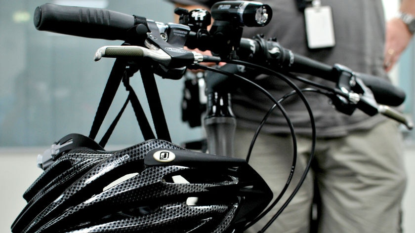 A bicycle rider stands next to a bike with a helmet hanging off the handlebars. (ABC News: Nic MacBean, file photo)