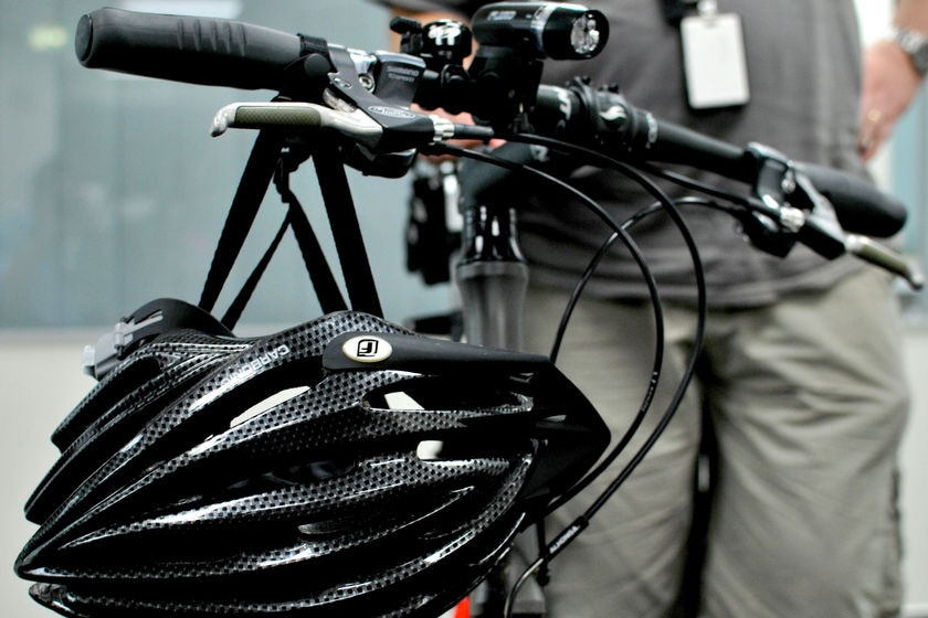 A black bike helmet hangs from the handlebars of a bike with a man standing in the background.