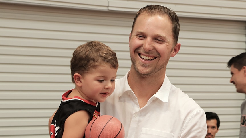 Tim Coenraad holds his son, who is holding a small basketball.