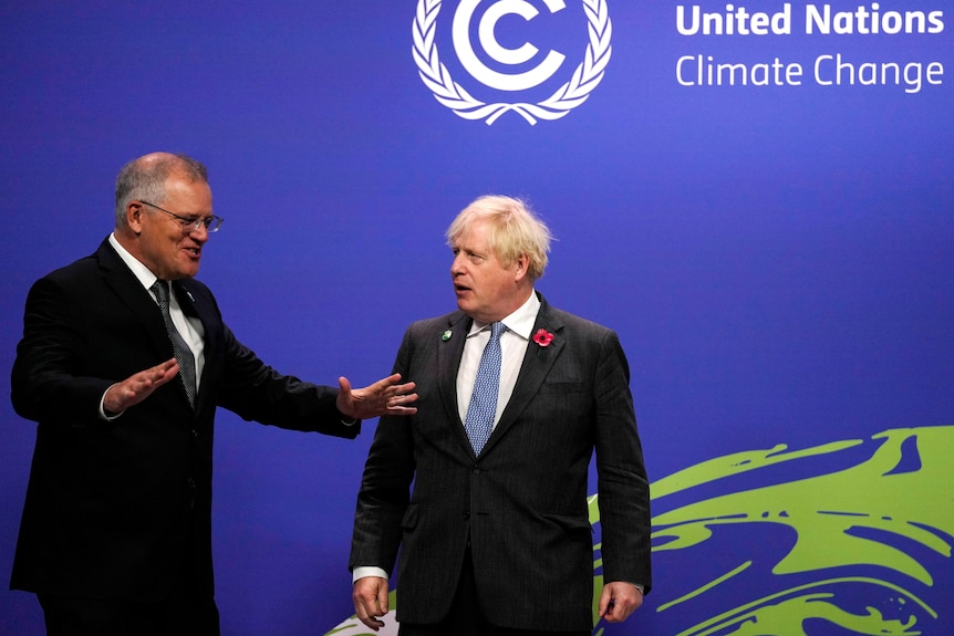 Scott Morrison talks and gestures with his hands and Boris Johnson looks at him.