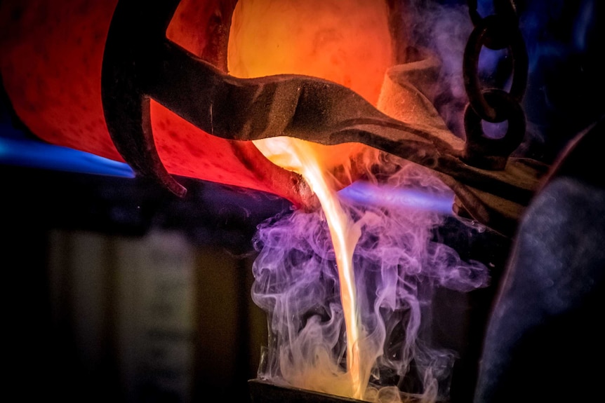 Liquid gold being poured out of a crucible held by tongs.
