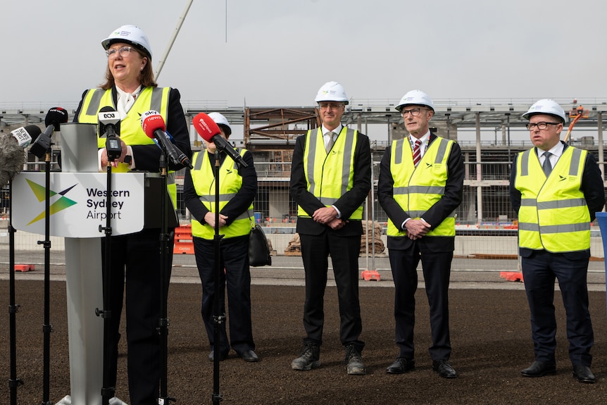 A woman wearing a hard hat standing behind a podium talking to the media.