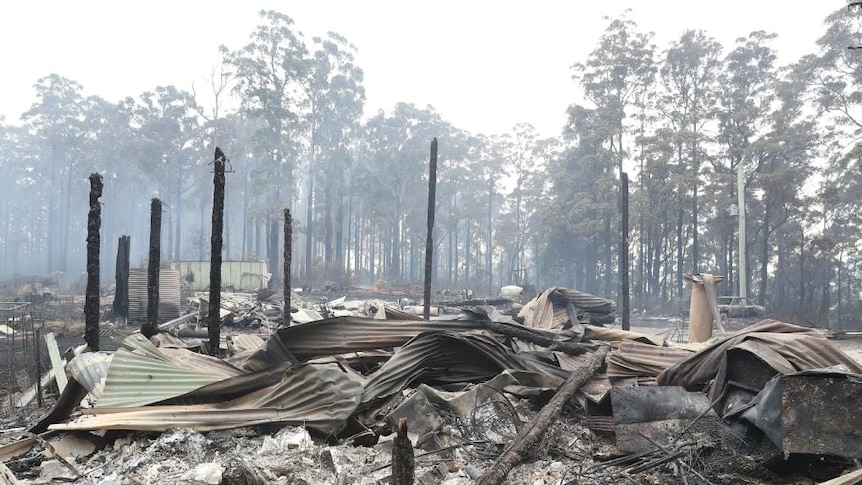 Charred poles and twisted roofing material sit among the remains of a house destroyed by bushfire.