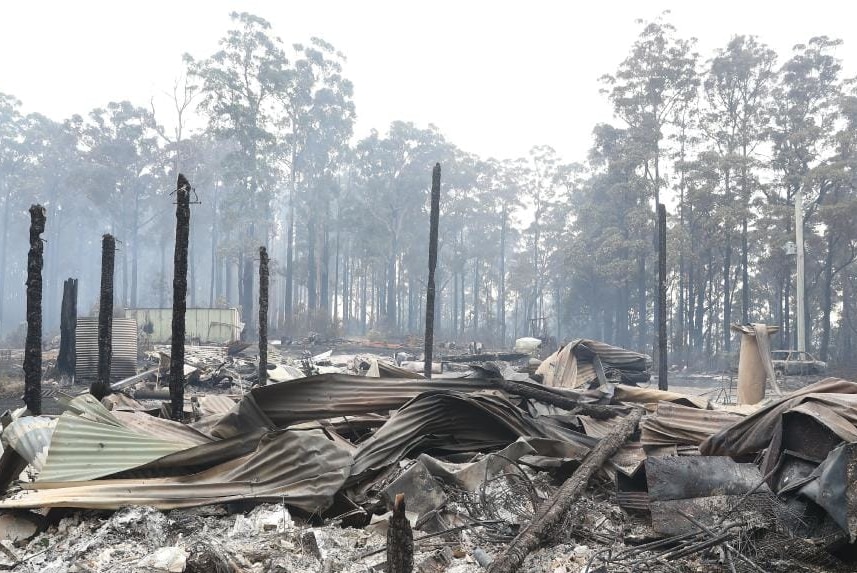Charred poles and twisted roofing material sit among the remains of a house destroyed by bushfire.