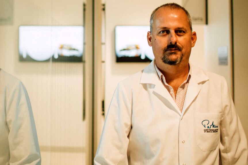 Professor Alistair Forrest stands in a laboratory dressed in a white lab coat.