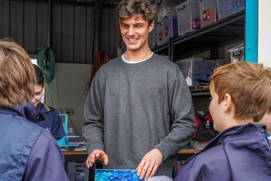 A young male teacher smiles at four short primary-aged kids.