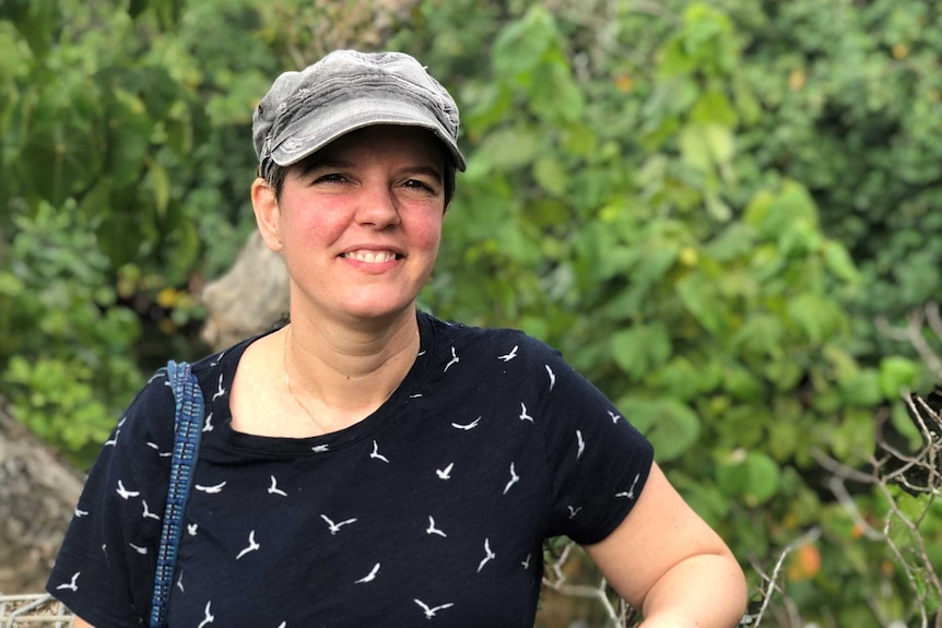 A birdwatcher smiles at the camera with birds in the background.