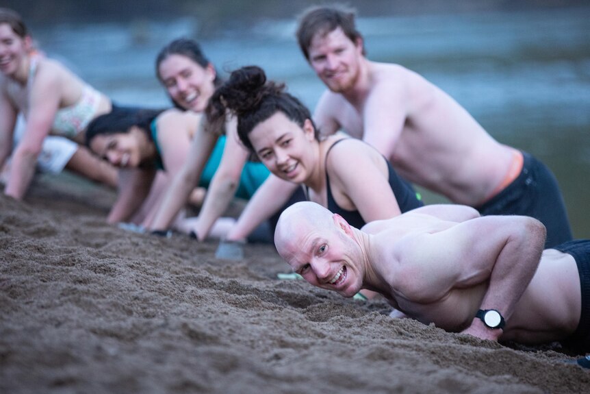David Pocock smiling while doing a pushup on a dirt riverbed in a line up of people 