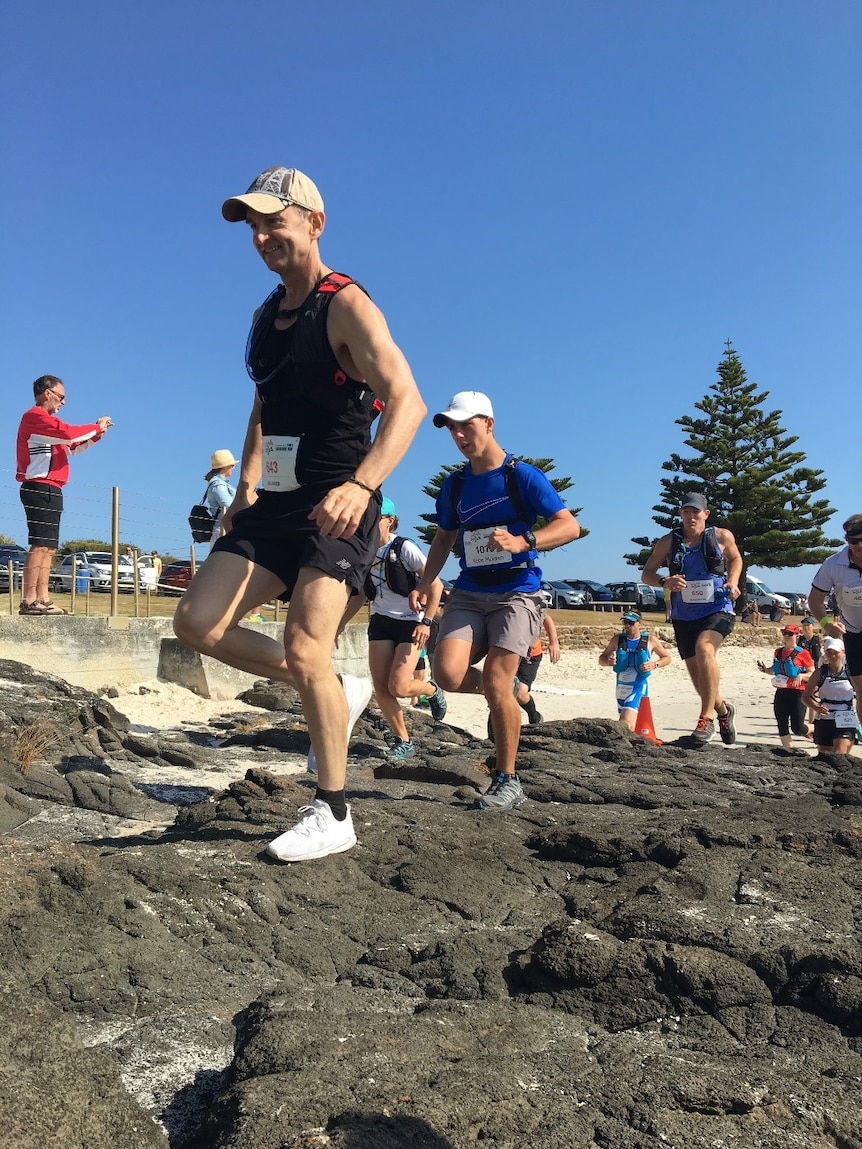 O'Brien and other runners running over rocks on beach.