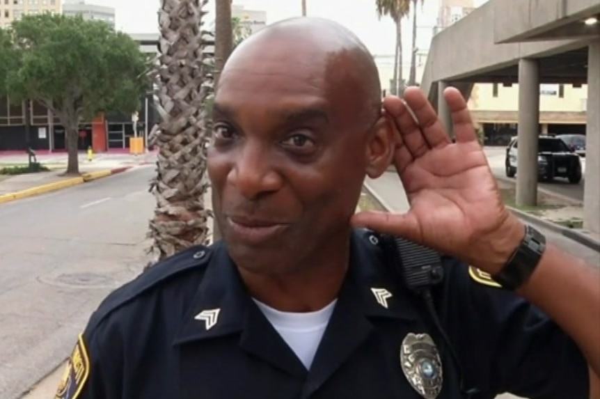 Senior Officer Richard Olden miming listening to shouts coming from inside an ATM.