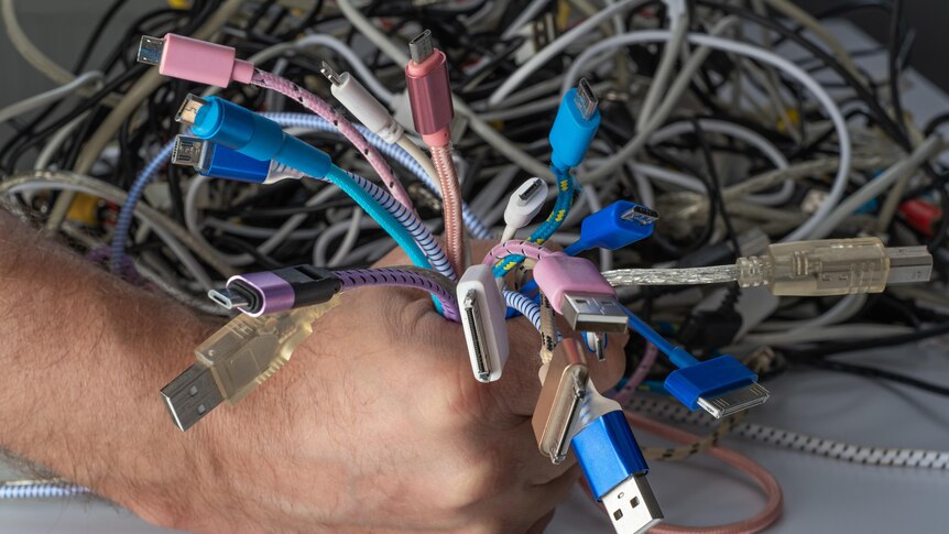 A fist clutching a wad of different coloured mobile phone leads and cables