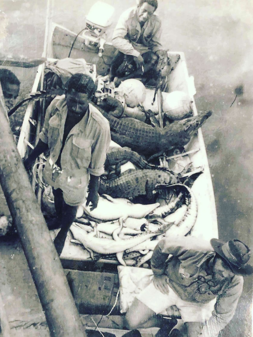 Black and white photo of three Papua New Guinean men and a Caucasian man on a boat with crocodile carcasses.
