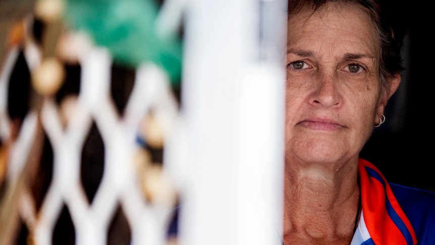 A woman peaks out of a screen door.