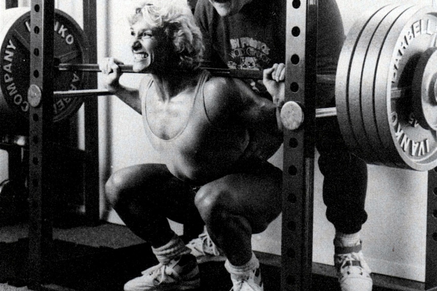 A woman squats down to lift a bar holding heavy weights.