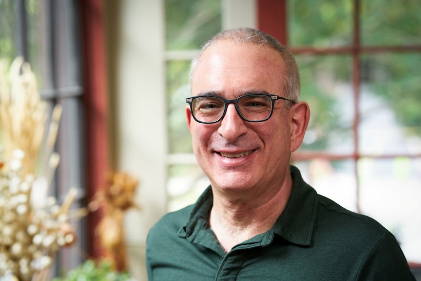 A man in a green shirt and black glasses smiles at the camera.