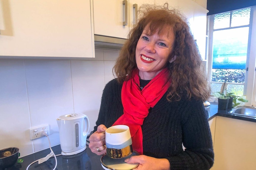 Carolina Williams smiles standing in a kitchen with a coffee cup.