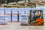 A woman drives a forklift inside a warehouse filled with toilet paper