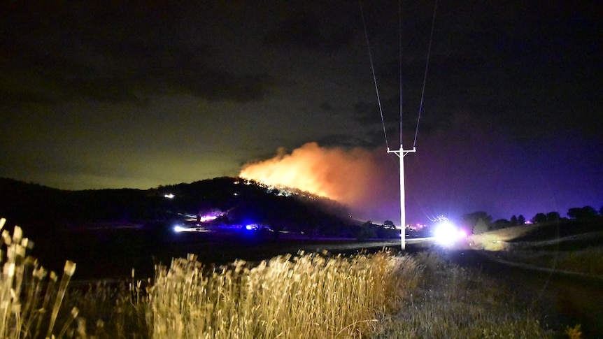 A grassfire burns on a distant hill at night time