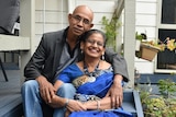 An older couple smiling and cuddling while sitting on the front steps of their home.