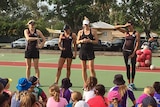 Firebirds players stands on a netball court, addressing seated children