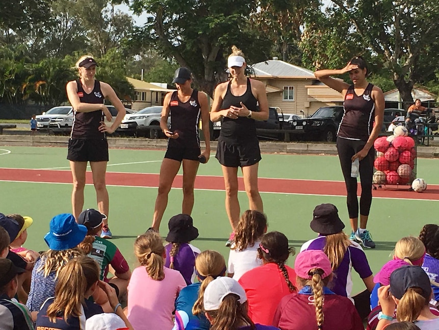 Firebirds players stands on a netball court, addressing seated children